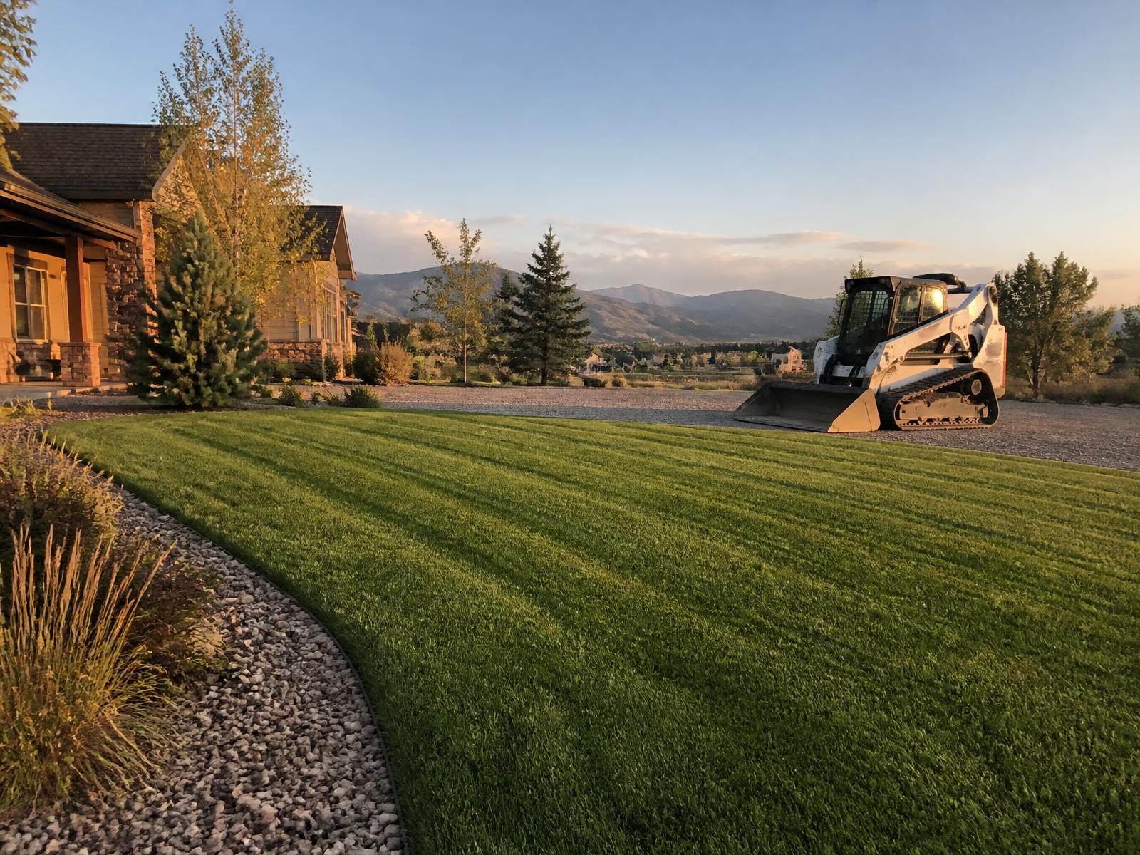 Freshly mowed lawn with a compact track loader on a gravel driveway